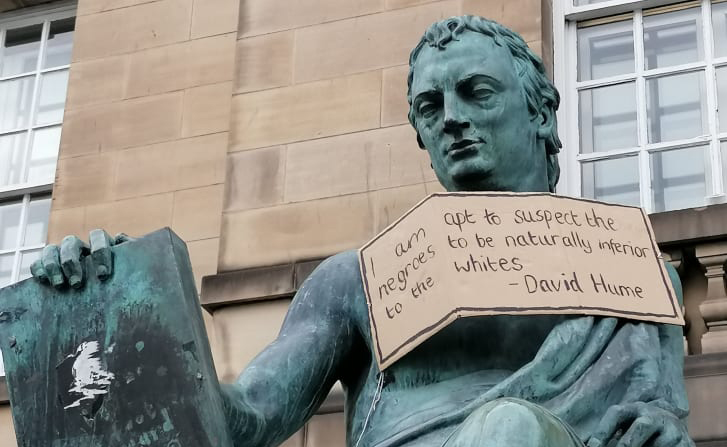 Socha Davida Humea v Edinburghu, 
na kterou aktivisté pověsili ceduli s úryvkem Humeovy „rasistické“ poznámky pod čarou. Zdroj: dailynous.com